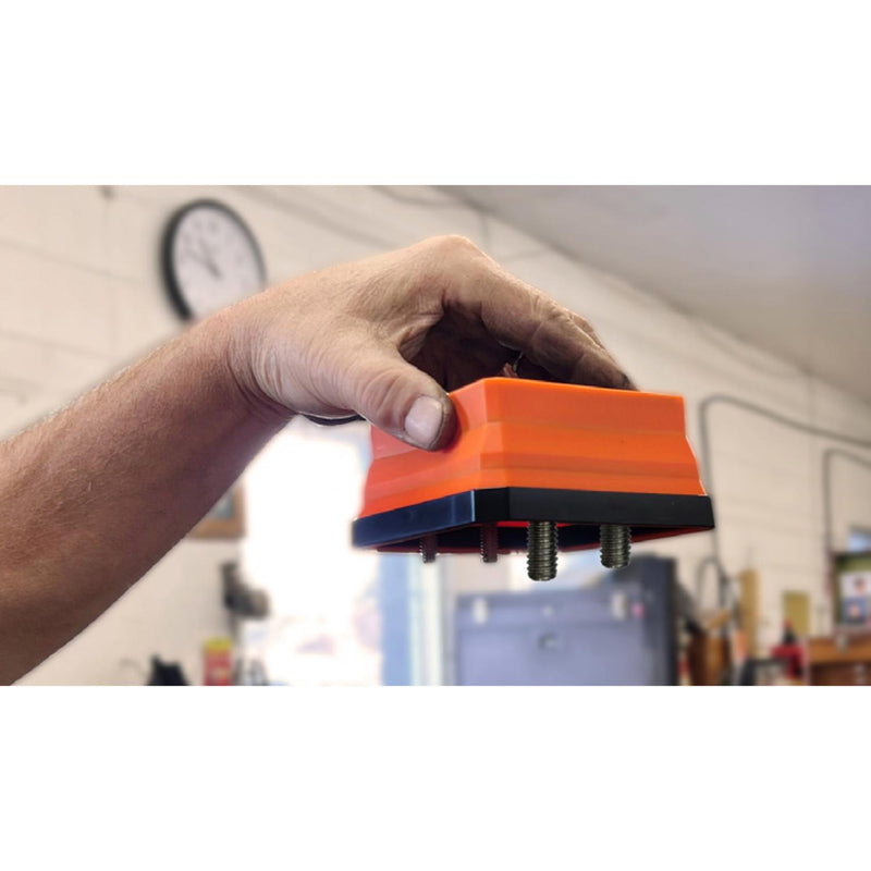 A hand holding an orange and black magnetic pop up tray upside down with three metal screws visible, set against a blurred workshop background to show the screws are not able to be tipped out